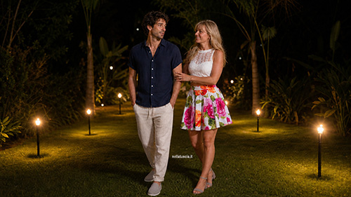 Marco e Livia camminano nel giardino illuminato del ristorante.